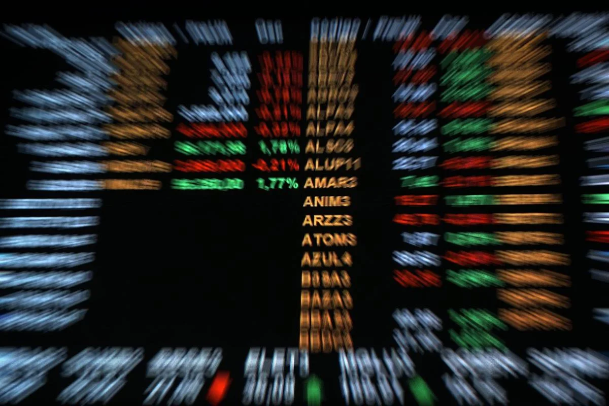 Imagem colorida desfocada do painel da Bolsa de Valores do Brasil, a B3, com os números que refletem o desempenho das ações negociadas